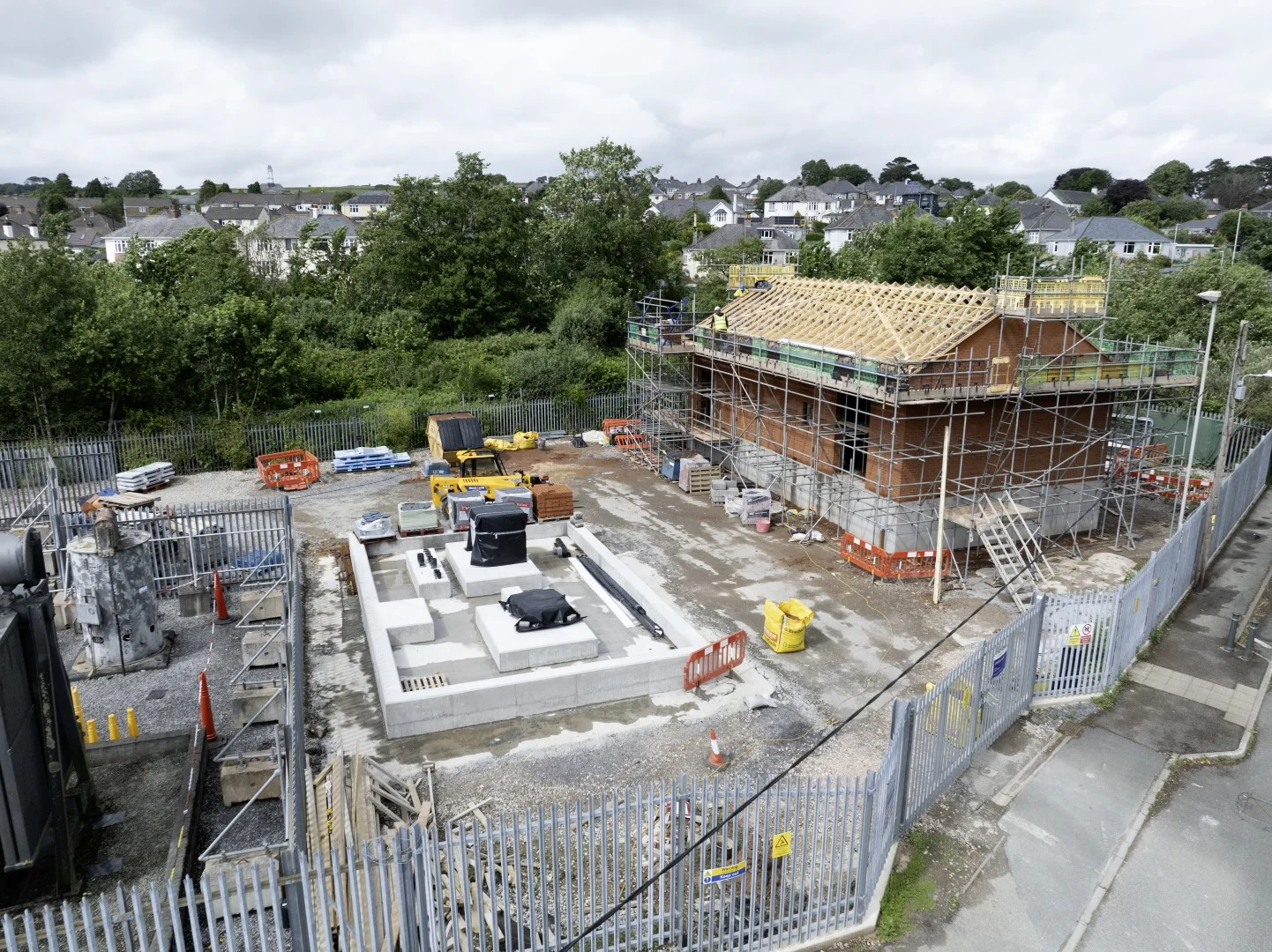 Construction site with concrete equipment foundations, scaffolding and a building with exposed timber roof framing