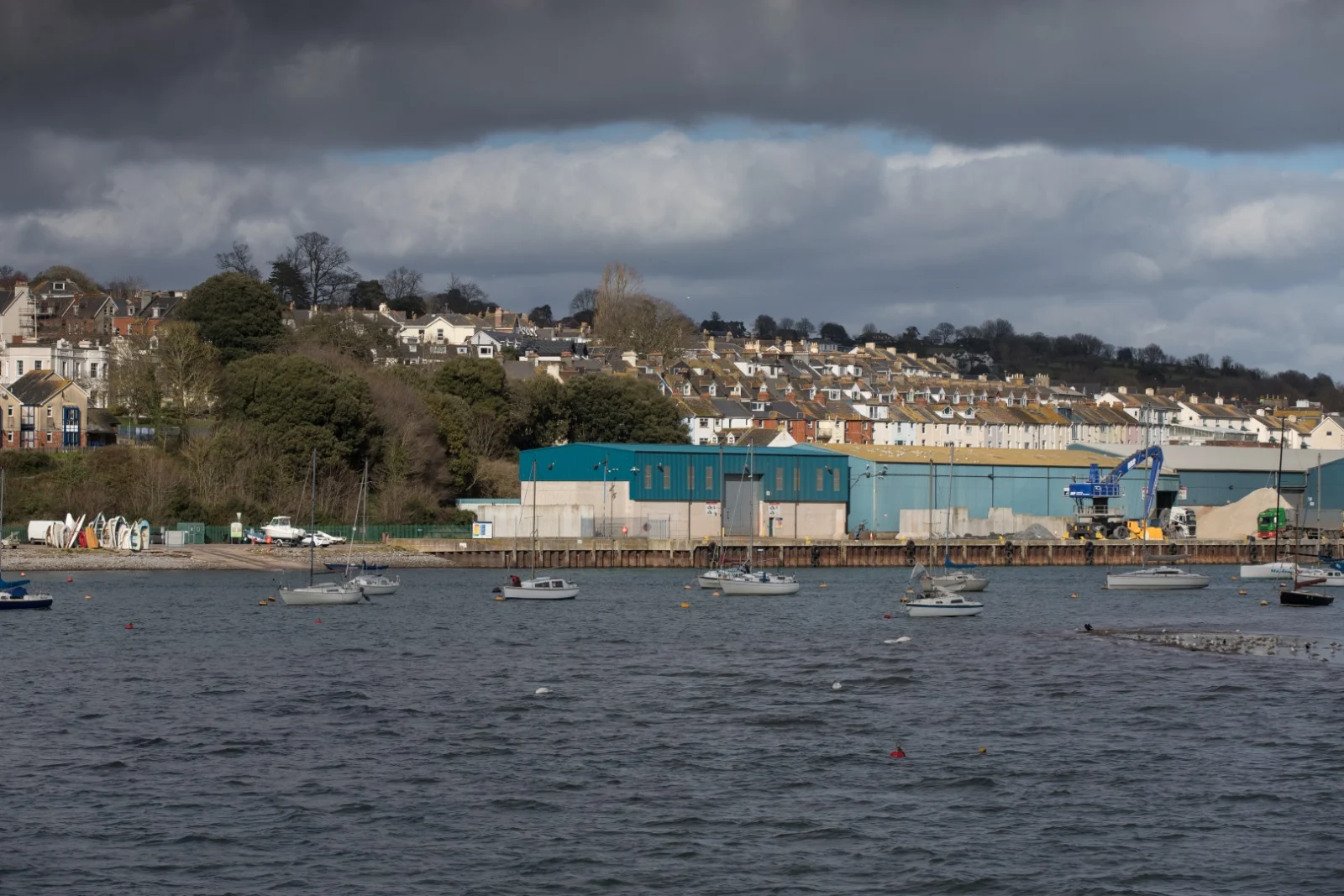 Industrial buildings and lifting equipment beside a quay, with boats in the foreground