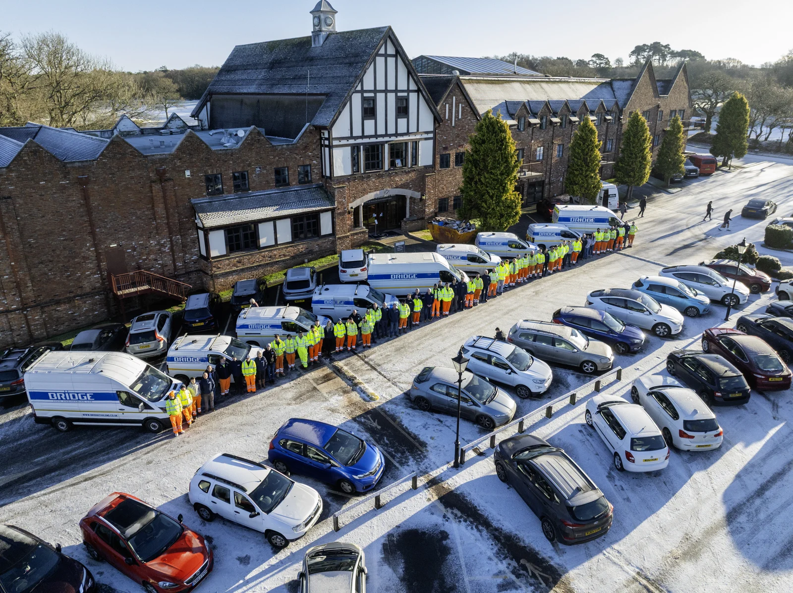 Aerial view of the Bridge team lined up beside company vans outside a building