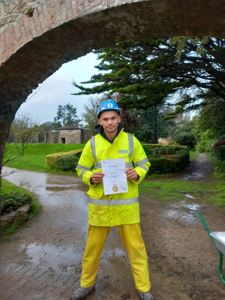 Josh Hemming in hi-vis and a hard hat on site, holding his Level 2 Groundworker certificate from Bridge Civil Engineering