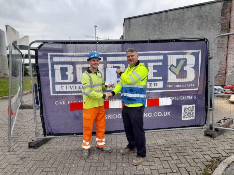 Tommy in hi-vis receiving his NVQ Level 2 certificate on site in front of a Bridge Civil Engineering banner