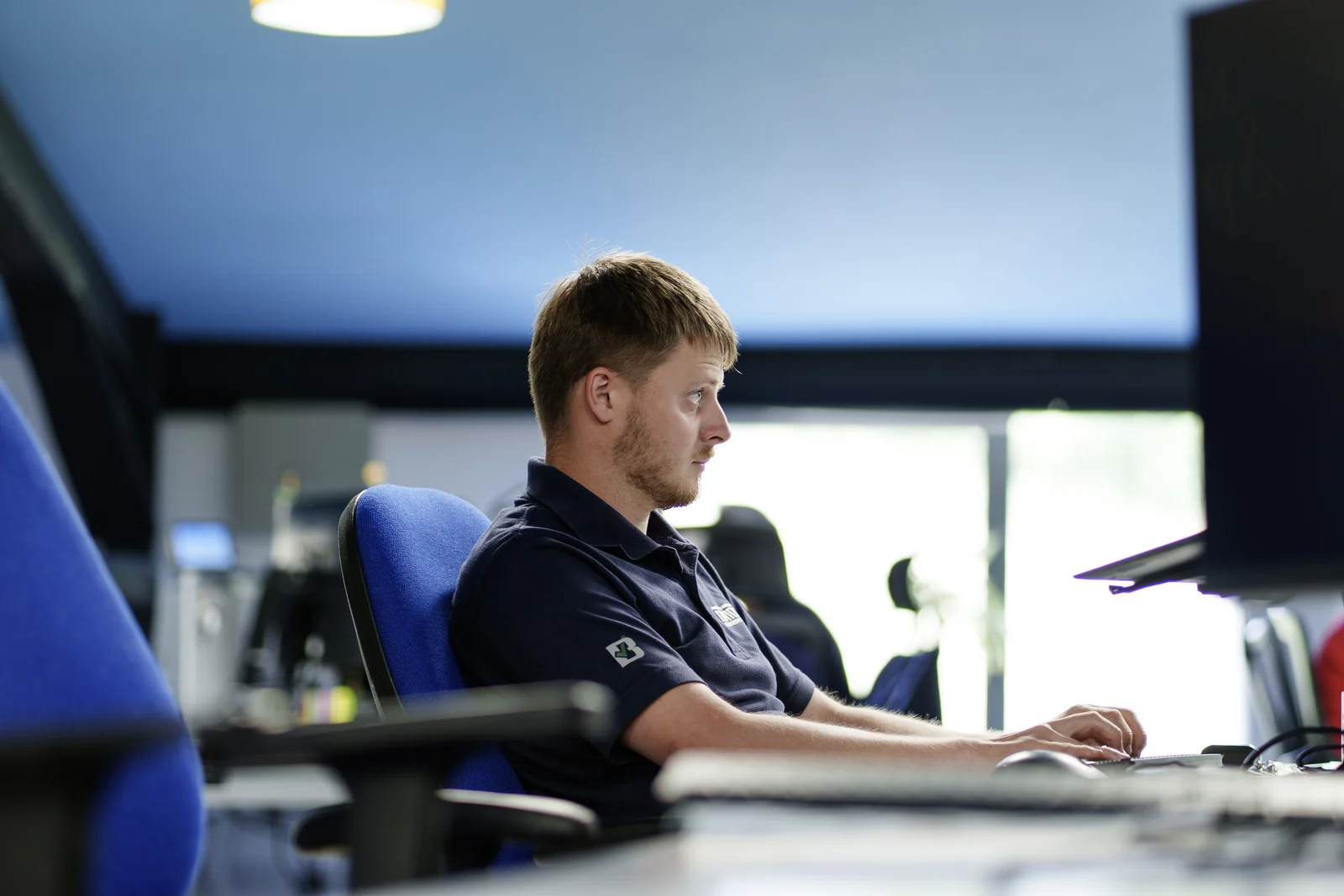 Bridge colleague in a navy company polo shirt working at a desktop computer in the office