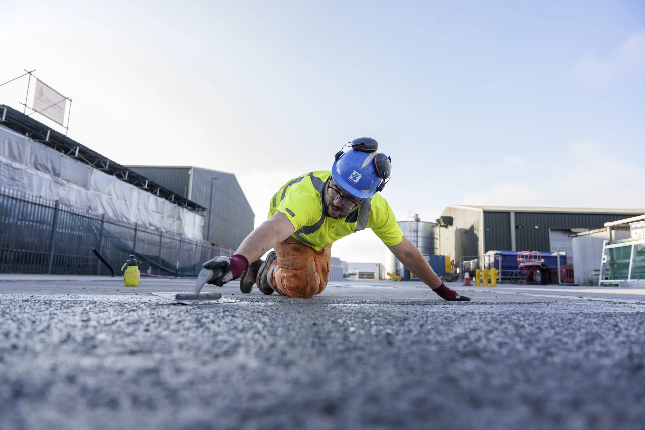 Bridge operative in a blue hard hat and high-visibility clothing using a hand trowel to finish a concrete surface