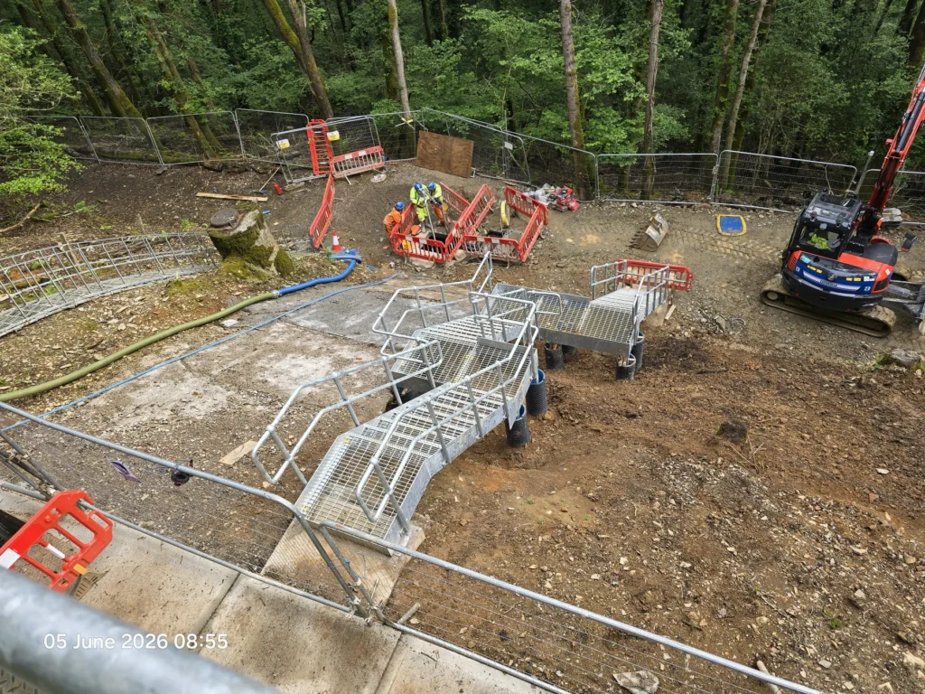 Glenholt Sewage Pumping Station upgrade works with metal access platforms, operatives and an excavator in a wooded site