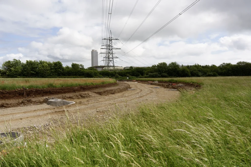 Earthworks and drainage chambers at Langage Energy Park, with an electricity pylon and industrial buildings beyond