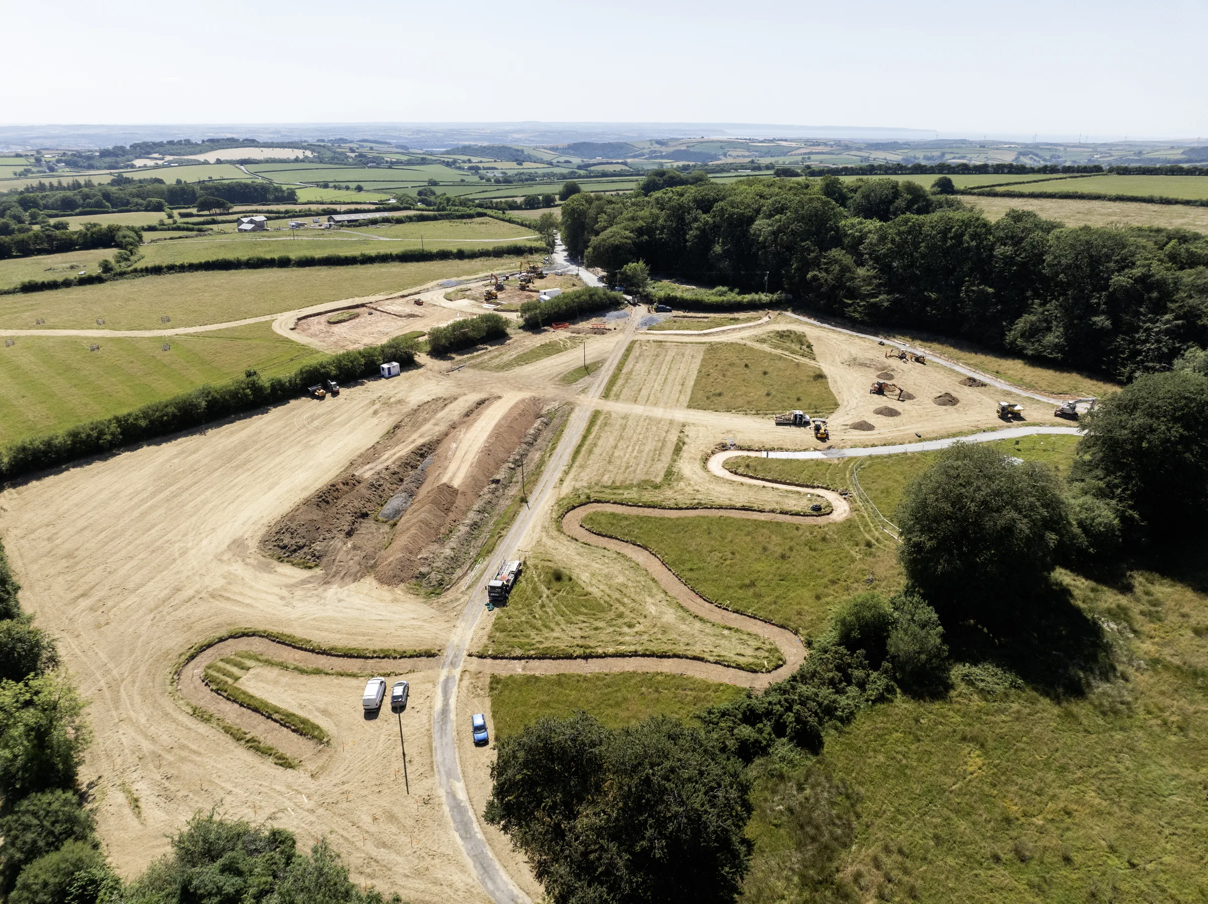 Aerial view of earthworks, construction machinery and access routes beside fields and woodland