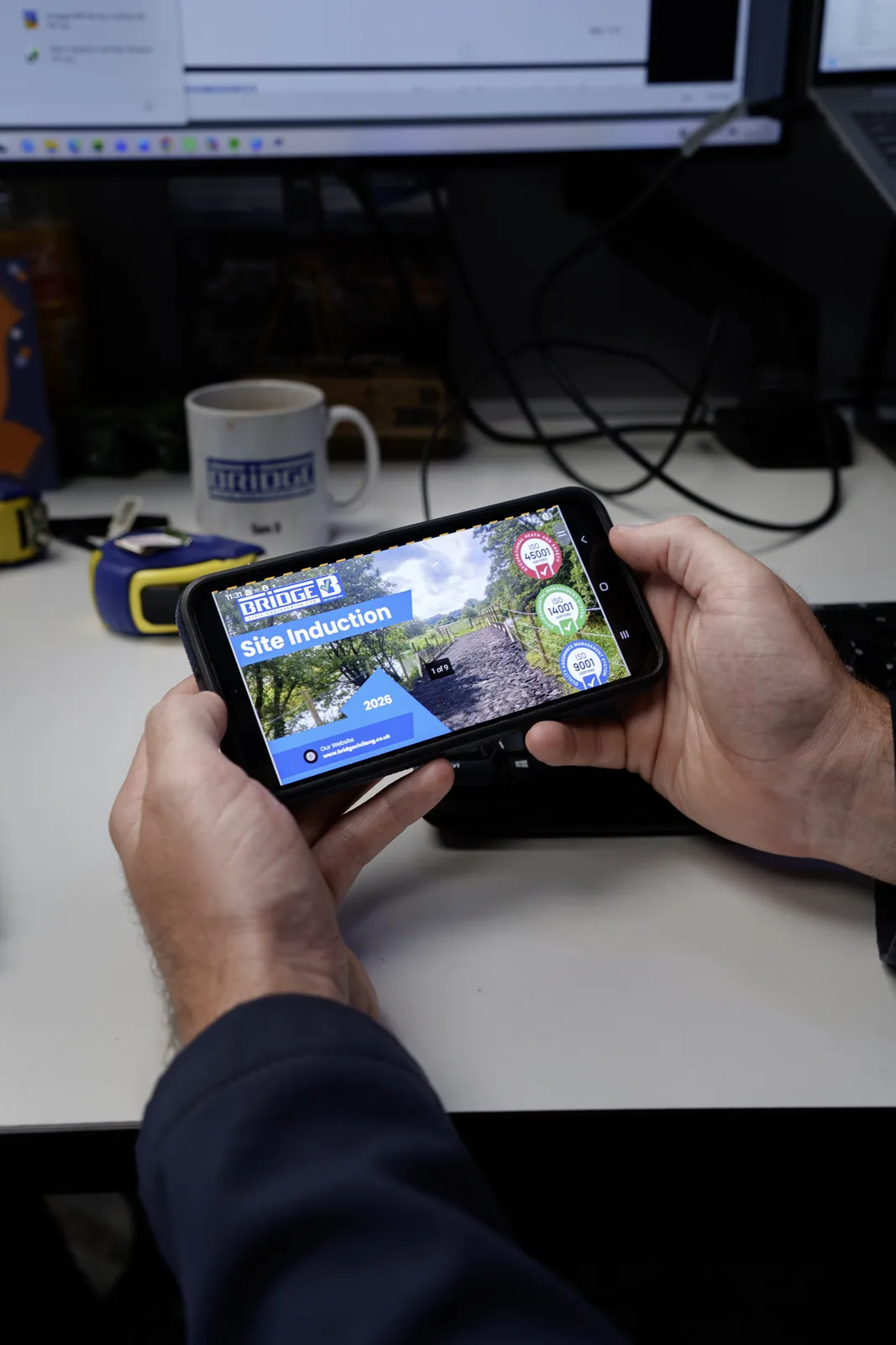 Hands holding a smartphone displaying the Bridge Civil Engineering digital site induction