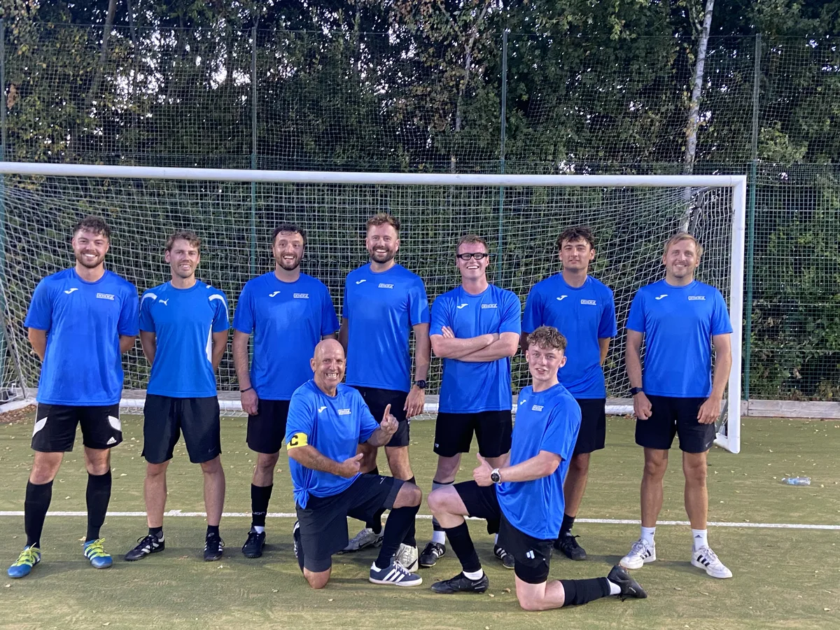 Nine people in blue Bridge shirts posing together in front of a football goal