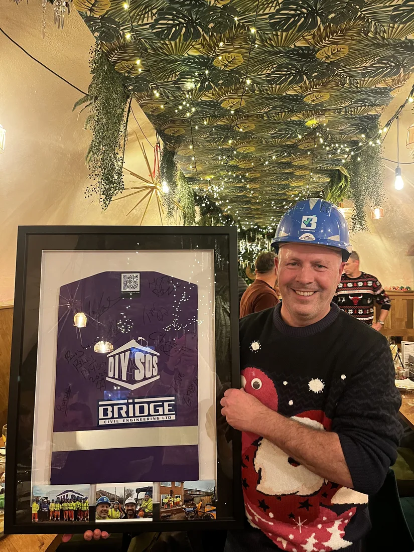 A Bridge colleague holding a framed, signed DIY SOS shirt and photographs