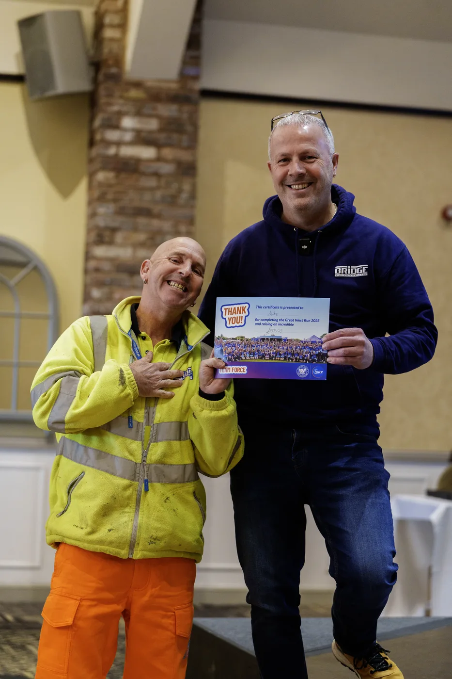 Two Bridge colleagues holding a FORCE charity thank-you certificate